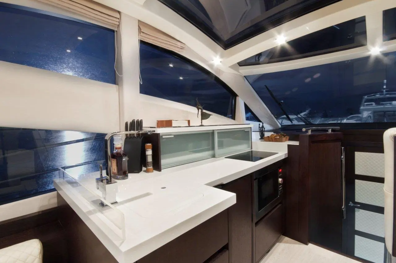 Modern boat kitchen with sleek surfaces, glass cabinetry, and night views of the marina through large windows.