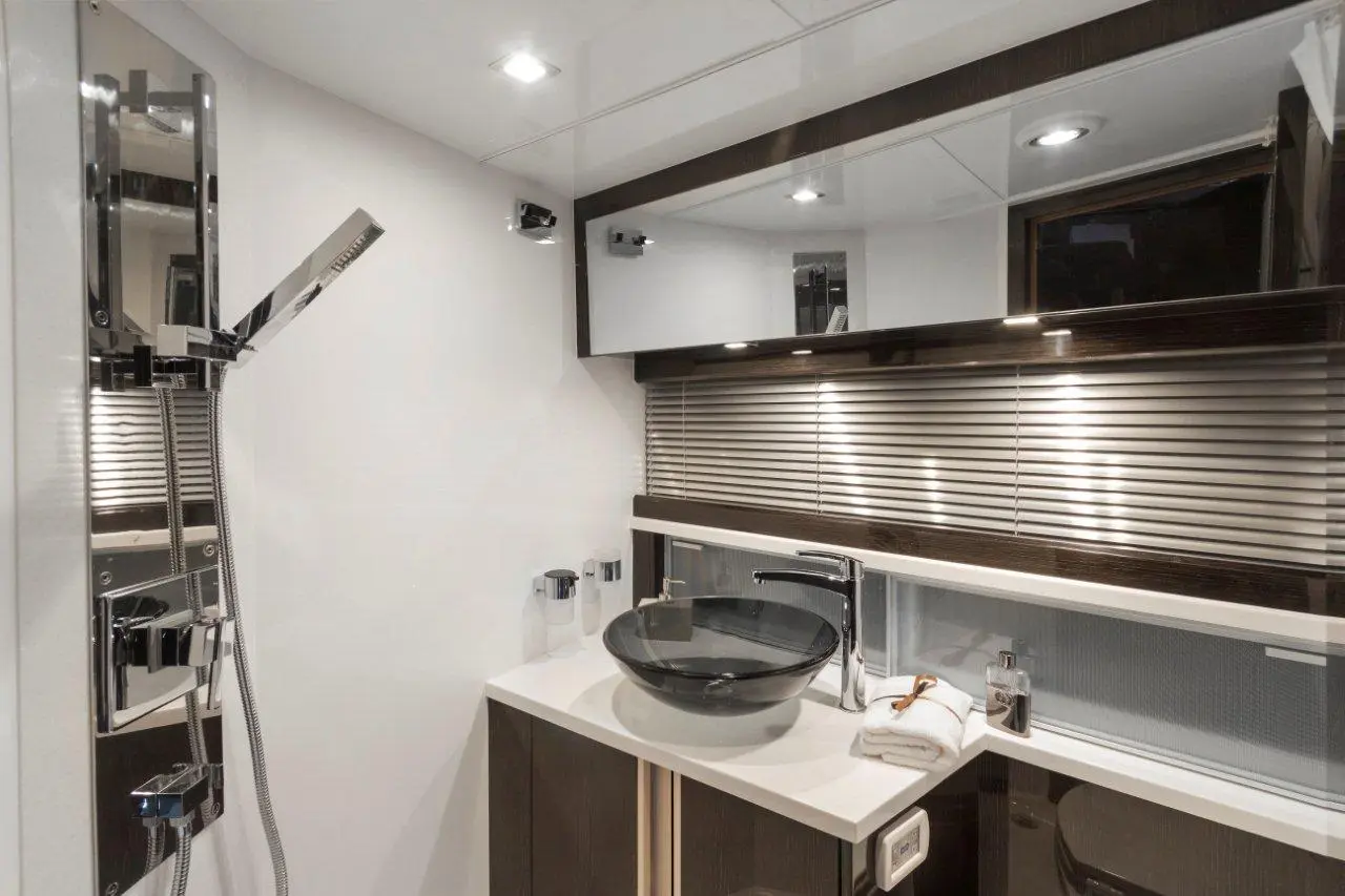 Modern bathroom featuring a sleek shower panel, glass basin, and wooden vanity with towels and decorative items.