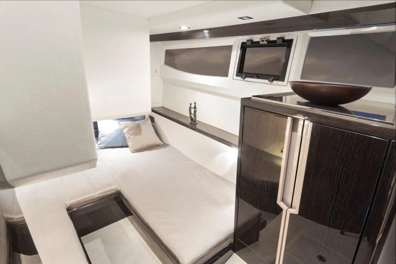 Modern yacht interior featuring a compact living area, a bed with pillows, a decorative statue, and a sleek cabinet.