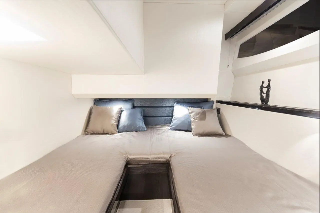 Modern bedroom with a double bed, grey and blue cushions, wall storage, and decorative figure on a shelf. Bright and minimalistic.