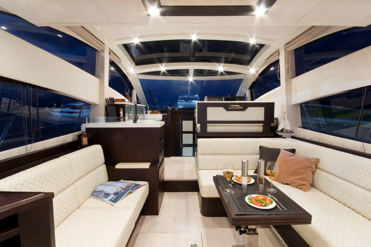 Modern yacht interior featuring a dining area, plush seating, and a table with plates of food and drinks, under soft lighting.