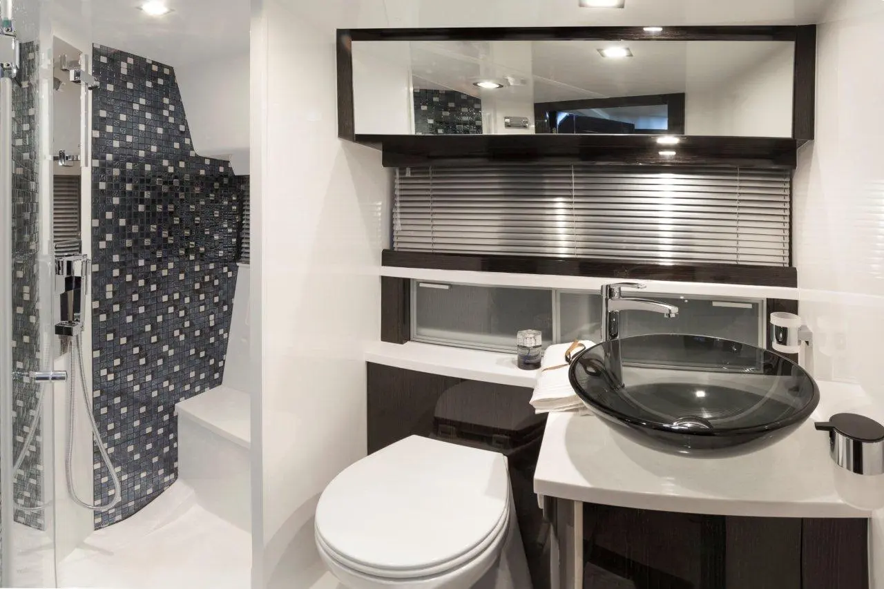 Modern bathroom featuring a walk-in shower with mosaic tiles, a sleek black bowl sink, and a white toilet against glossy surfaces.