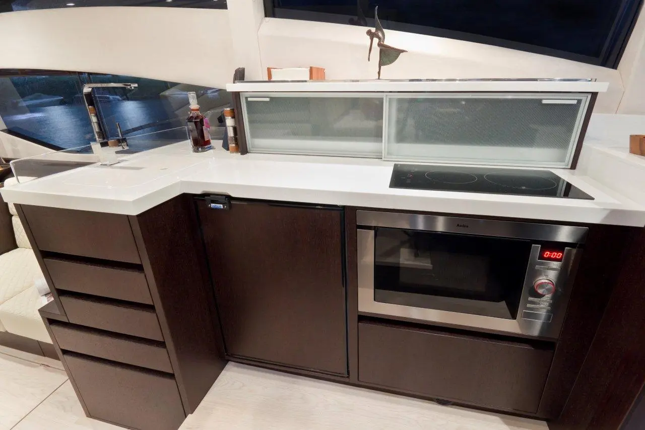 Modern kitchen with dark wood cabinets, white countertop, microwave, induction cooktop, and a view of water through large windows.