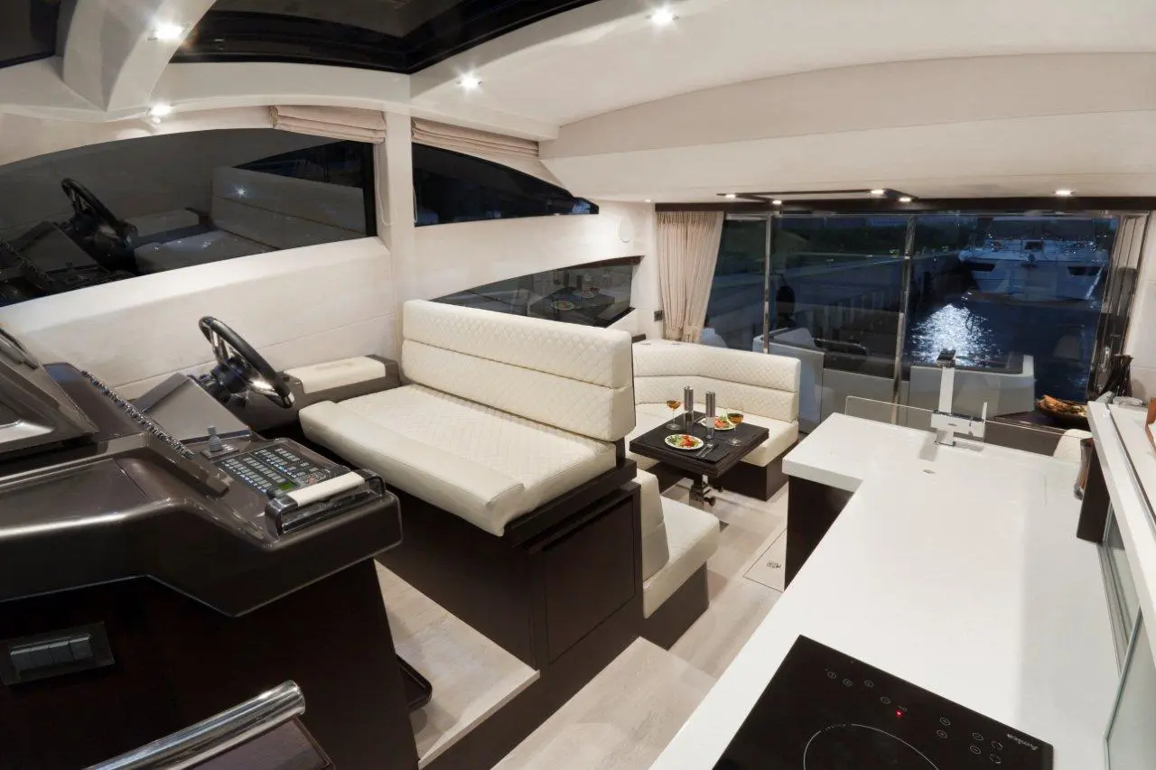 Luxury yacht interior featuring a modern helm, seating area, and dining table with food, overlooking a serene marina.
