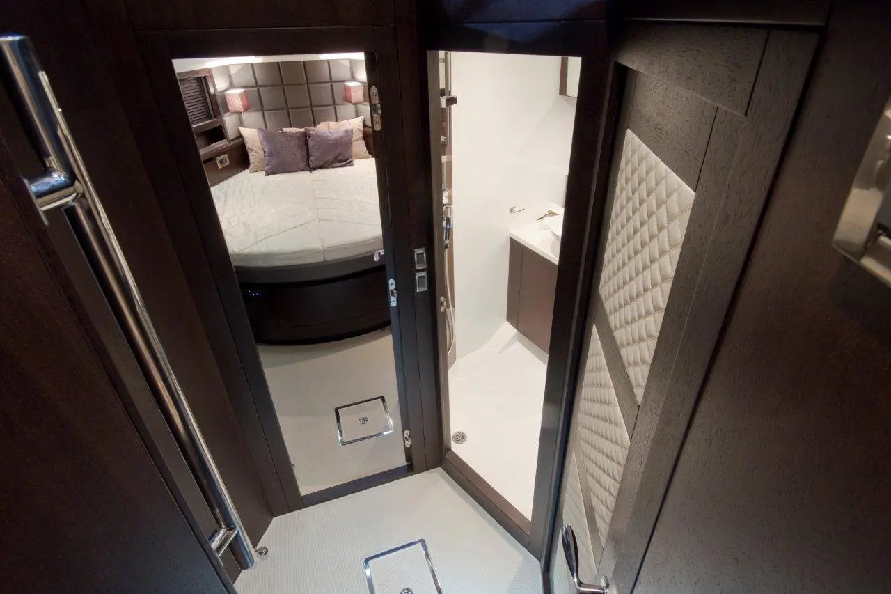 Interior view of a luxury yacht cabin showing a round bed, bathroom door, and modern furnishings in dark wood tones.