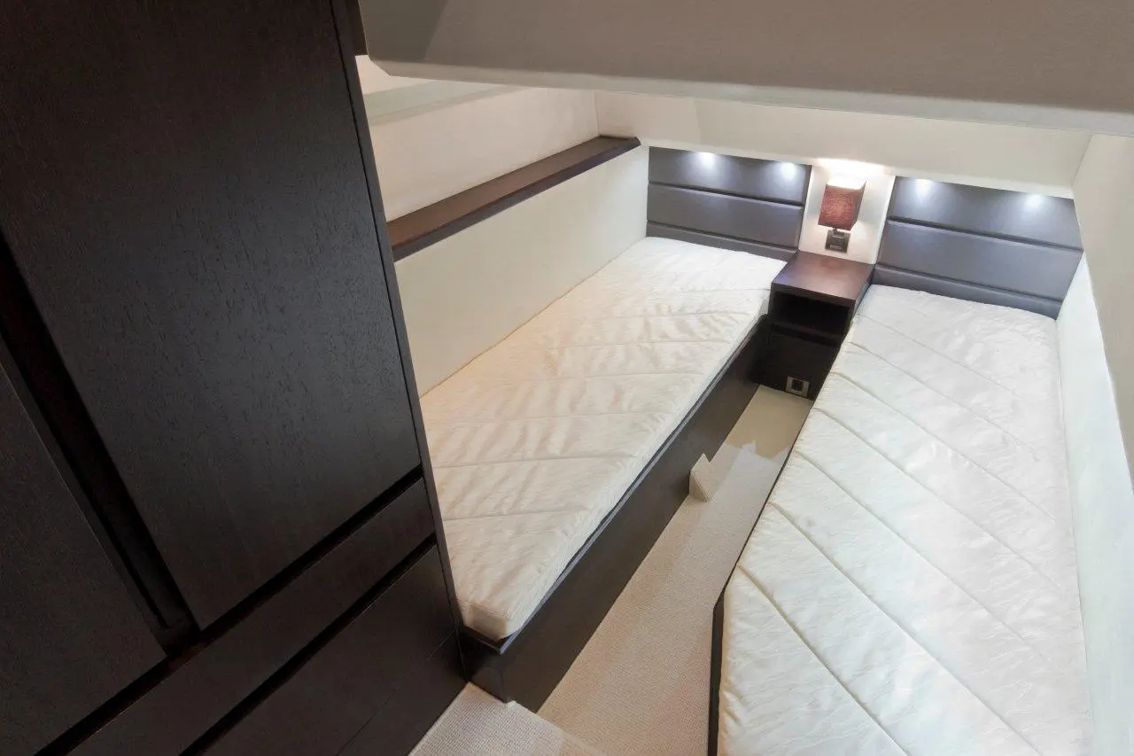 Compact twin bedroom with two single beds, dark wood furniture, soft lighting, and neutral-coloured walls.