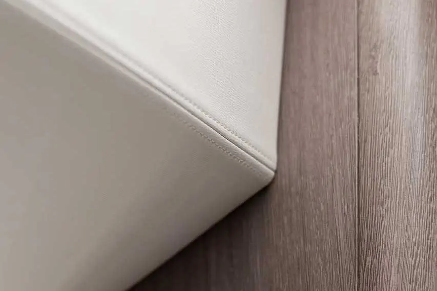 Corner of a white upholstered item against a textured wooden surface, highlighting its clean lines and minimalistic design.