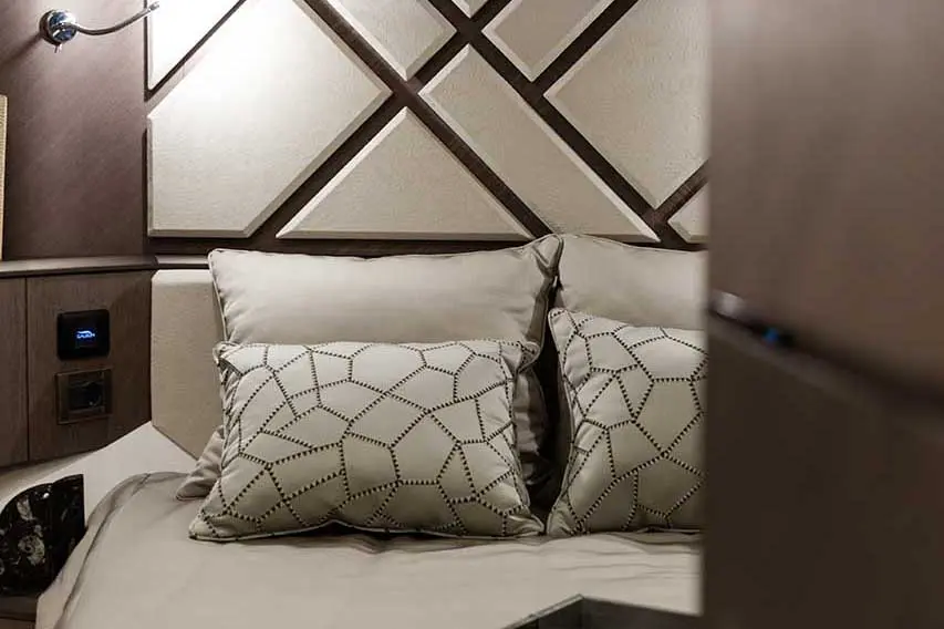 Cozy bedroom scene featuring a bed with decorative pillows, a textured wall, and bedside control panel.