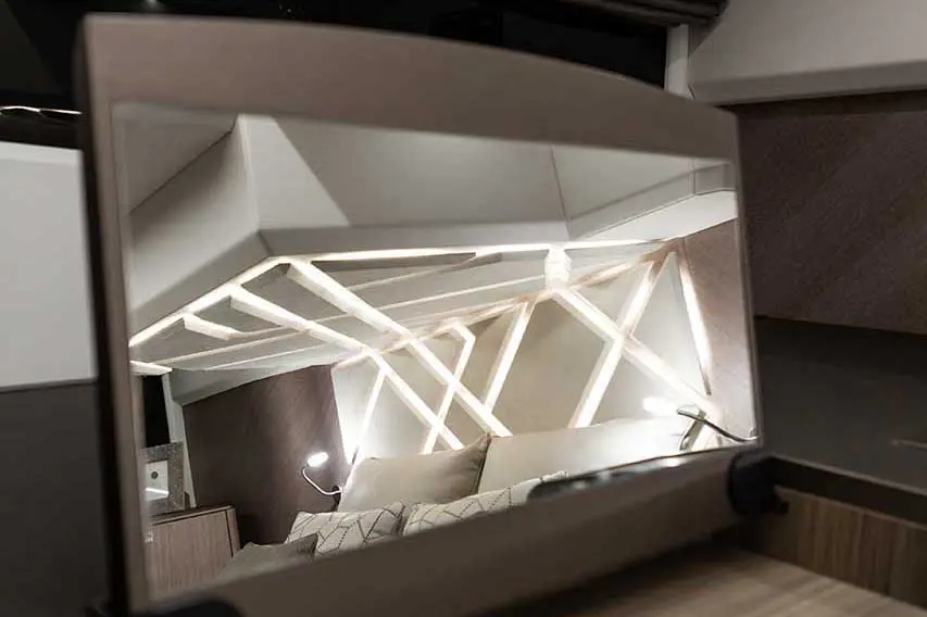 Reflection in a modern mirror showcasing a cozy bedroom with geometric LED lighting and a neatly made bed.