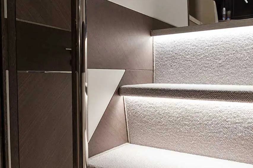 Illuminated staircase with textured carpet, modern wooden panels, and sleek metal railing, highlighting contemporary design.