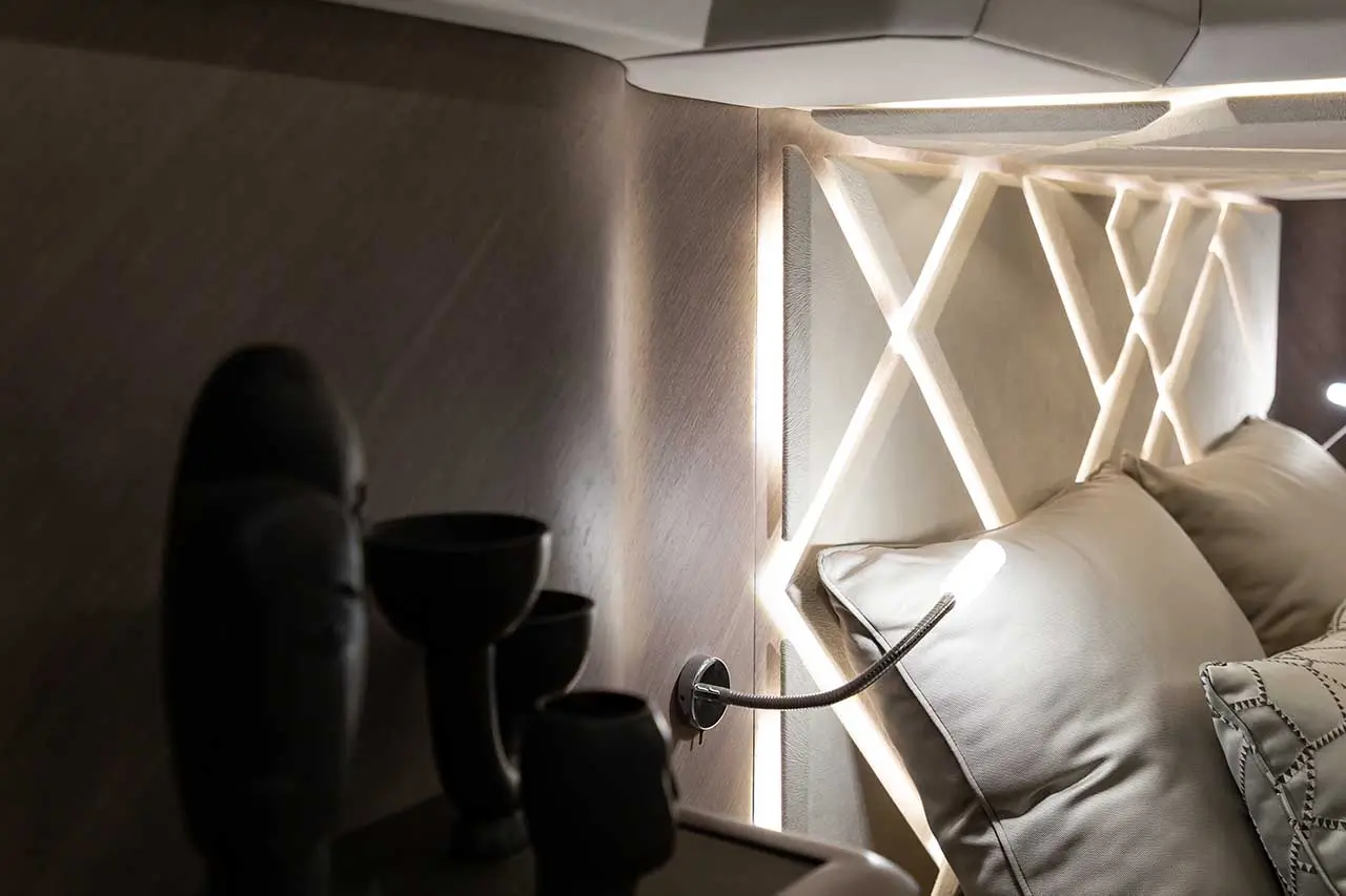 Modern bedroom corner featuring elegant pillows, decorative wall with backlighting, and minimalist black vases.