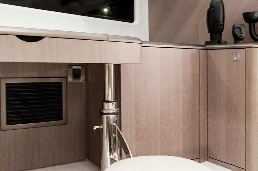 Modern interior with wooden cabinets, a silver pipe, and decorative sculptures on a shelf. Subtle textures and colors present.