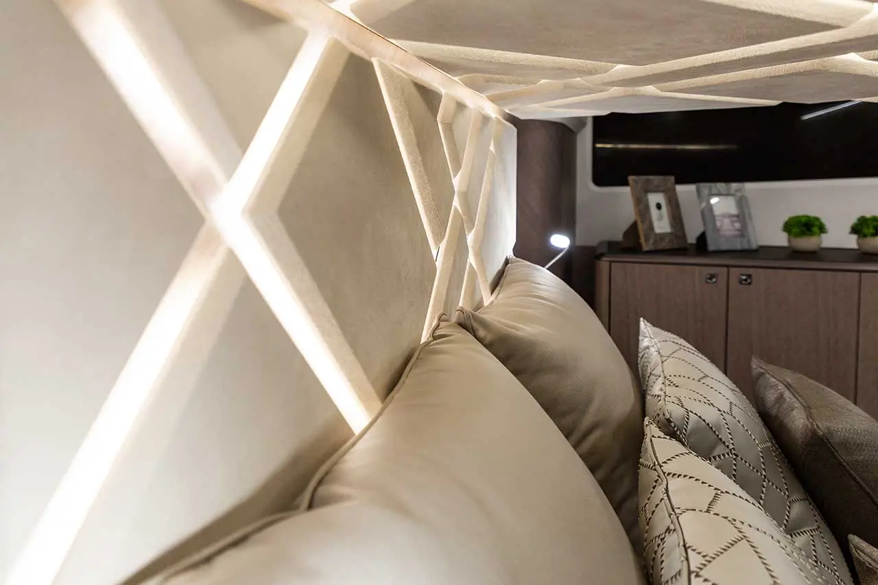 Cozy interior with illuminated geometric wall design, beige cushions, and a wooden cabinet displaying framed photos and plants.