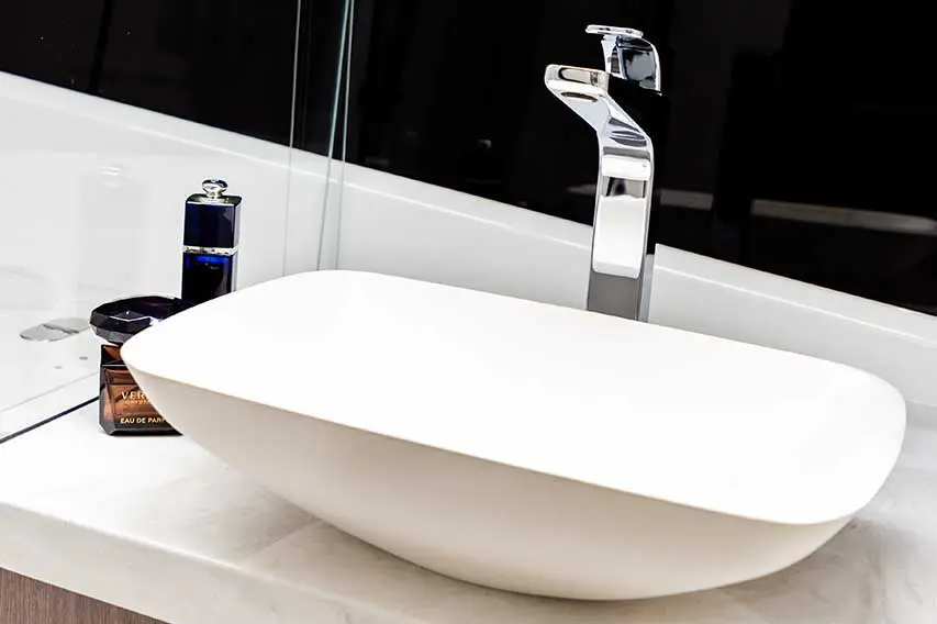 Modern bathroom sink featuring a white basin, chrome faucet, and fragrance bottles on a marble countertop.