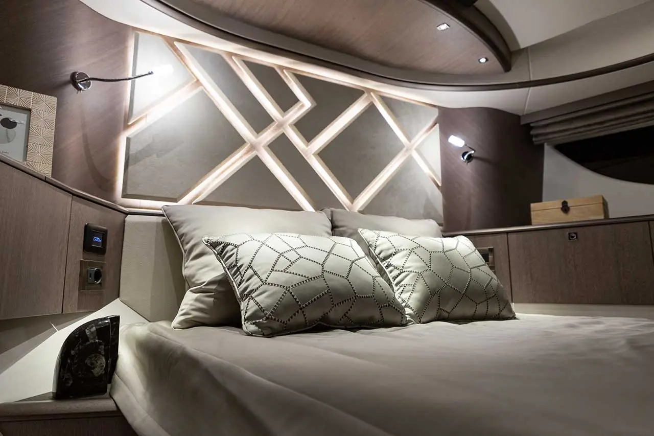 Elegant bedroom showcasing a bed with patterned pillows, warm lighting, and modern decor; features stylish wooden accents.