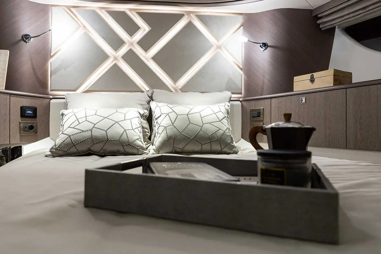 Cozy bedroom with decorative pillows on a bed, a tray with a coffee pot and books, and stylish wall lighting.