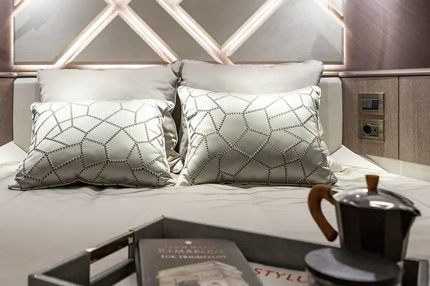 Stylish bed with two decorative pillows, a tray with a coffee pot, and a book, against a softly lit headboard.