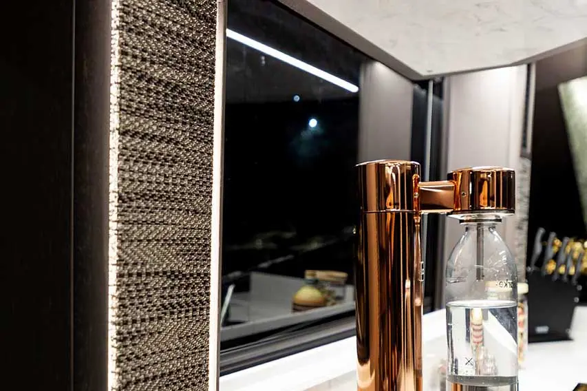 Modern kitchen featuring a bronze water dispenser and a clear bottle on a counter, with a textured wall accent and window.