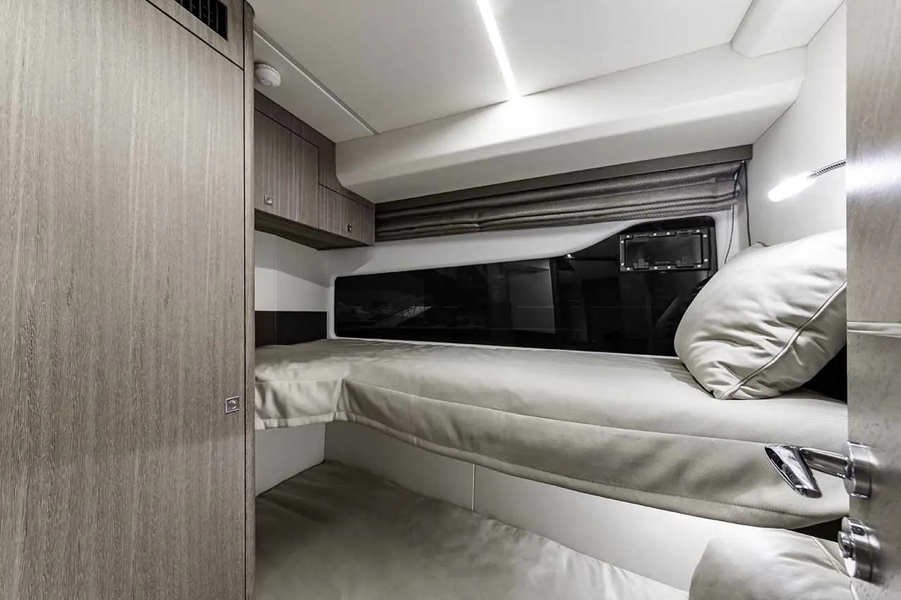 Interior view of a modern boat cabin, featuring a cozy bed, wood paneling, and a large window for natural light.