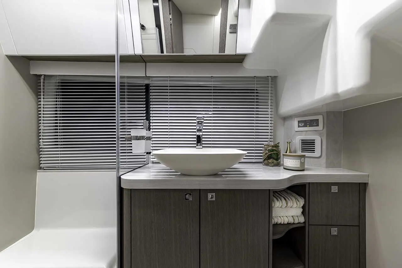 Modern bathroom featuring a sleek white sink, wooden cabinets, and neatly stacked towels under a window with blinds.