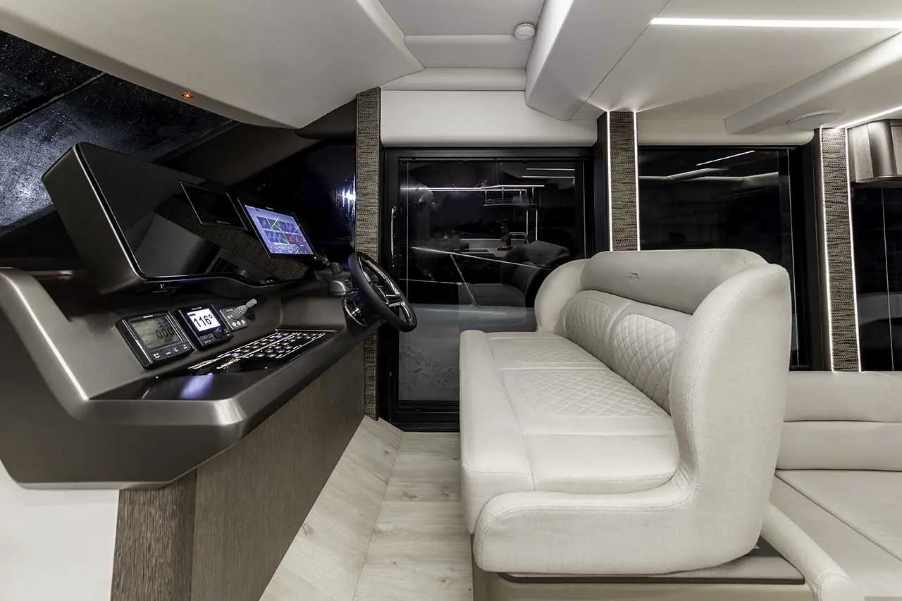 Modern yacht interior featuring a control panel, steering wheel, and a plush seating area with large windows.