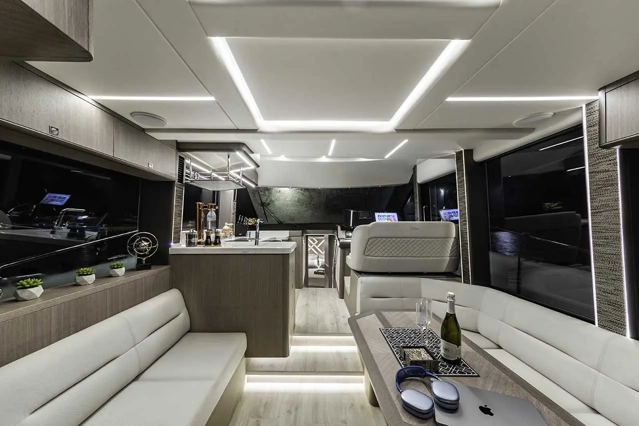 Modern yacht interior featuring a sleek lounge area, elegant lighting, a bar, and windows displaying night views.