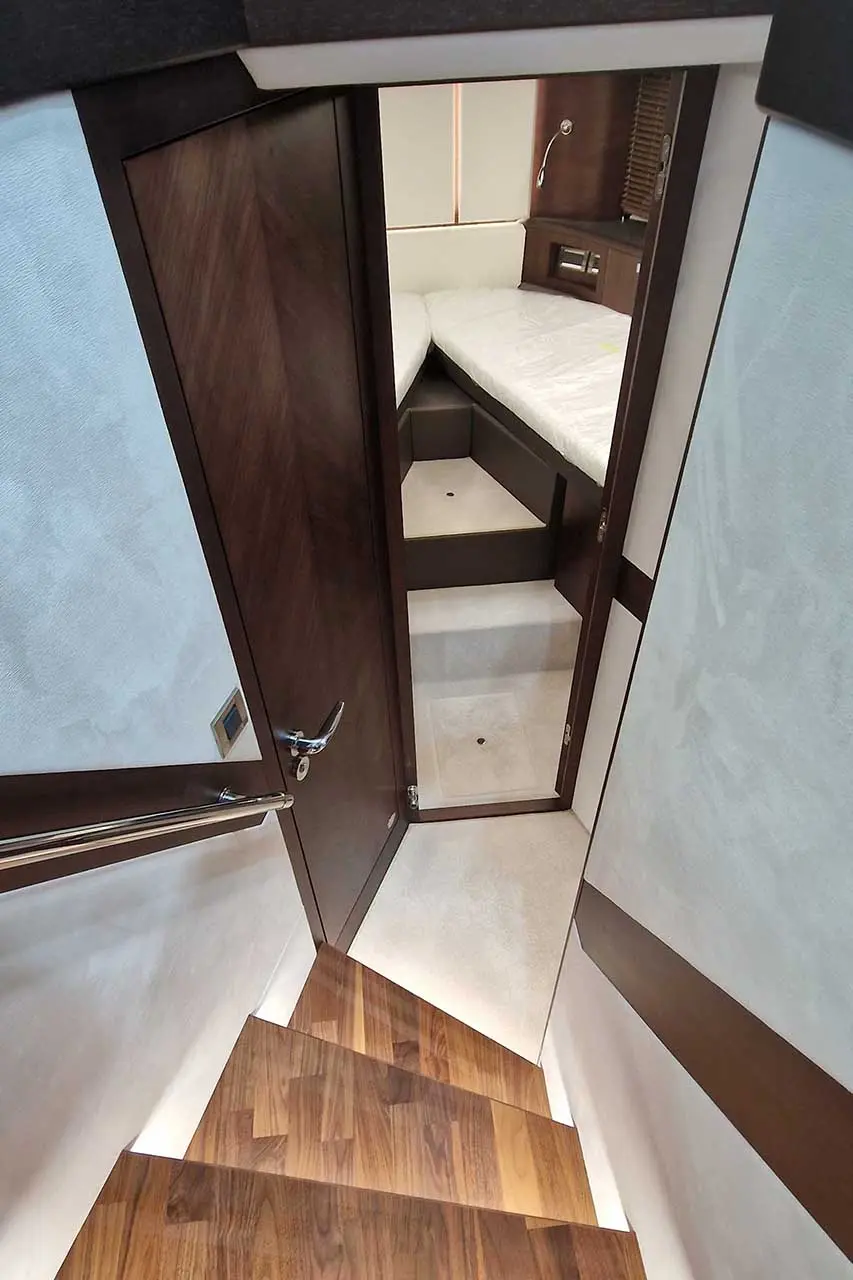 Interior view of a boat showing a staircase leading to a small cabin with twin beds and wooden accents.