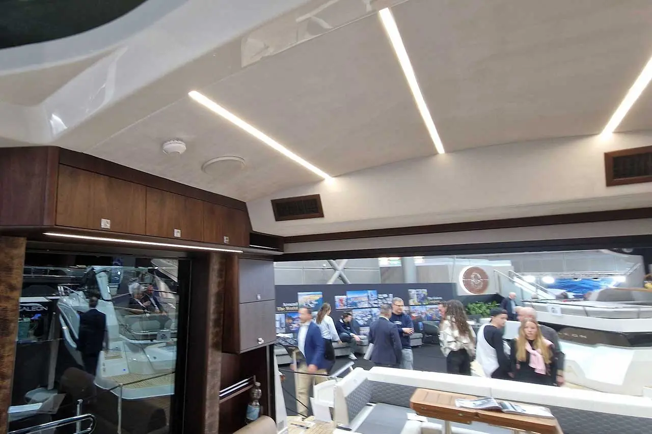 Interior view of a modern boat featuring wood accents, overhead lighting, and people gathered near boat displays.