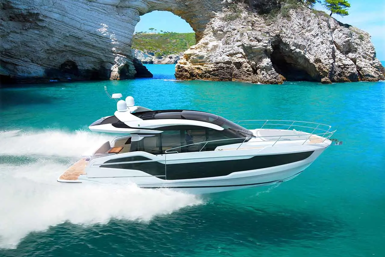 A sleek white yacht speeds through turquoise waters, approaching a rocky coastal arch on a sunny day.