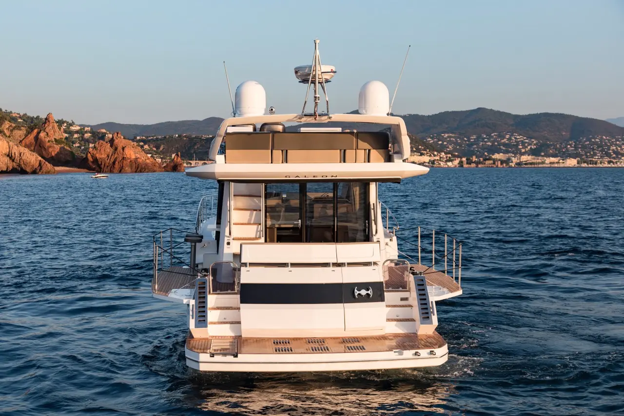 Luxury yacht Galeon cruising on calm waters, with rocky coastline and hills in the background illuminated by sunset.