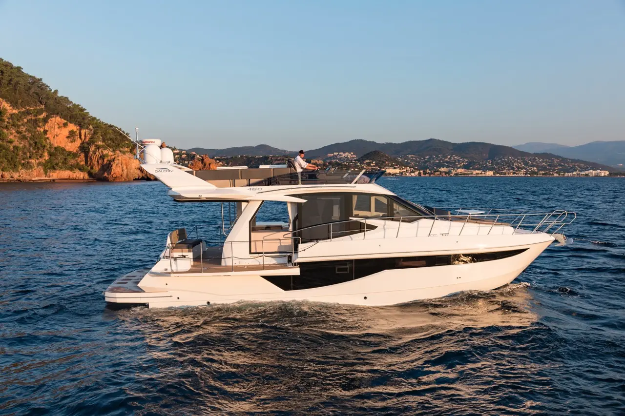 Luxury yacht navigating calm waters near a rocky coastline at sunset, showcasing sleek design and modern features.