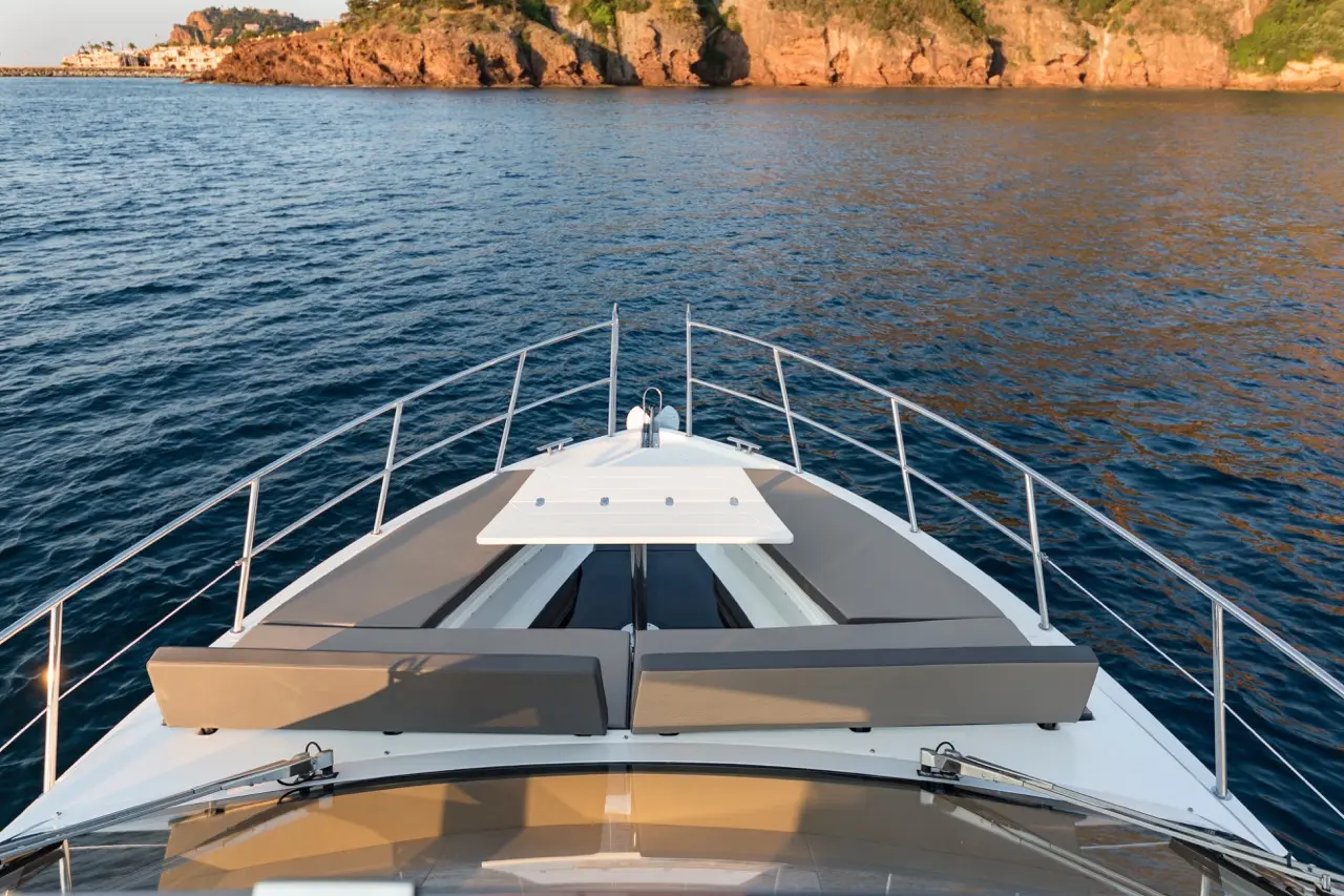 View from the bow of a luxury yacht, featuring gray seating and a panoramic waterfront of rocky cliffs and calm waters.