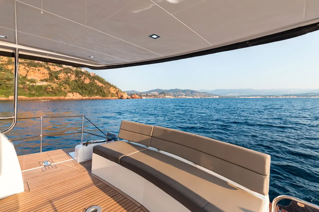 Luxury yacht with a spacious bench, overlooking calm waters and a scenic coastline under clear skies.