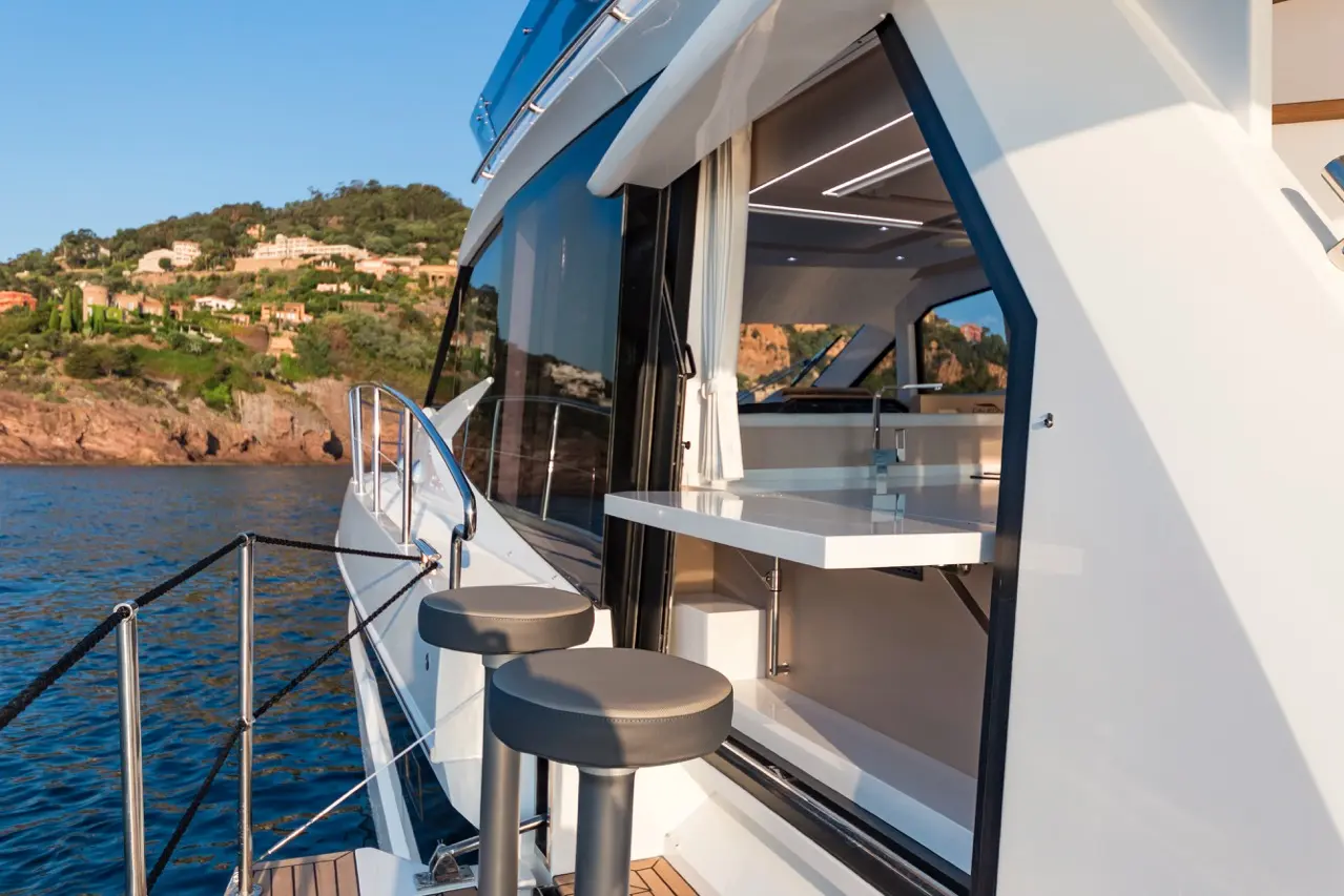 Modern yacht exterior with a sleek design, featuring a view of the ocean and hillside. Includes two bar stools by a counter.