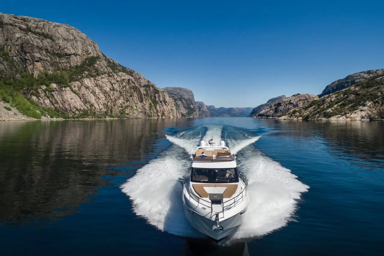 Luxury motorboat gliding through calm water, flanked by rocky cliffs and lush greenery under a clear blue sky.