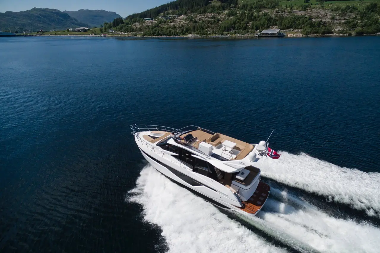 Luxury yacht speeds across a serene blue lake, leaving a wake behind, with green hills visible in the background.