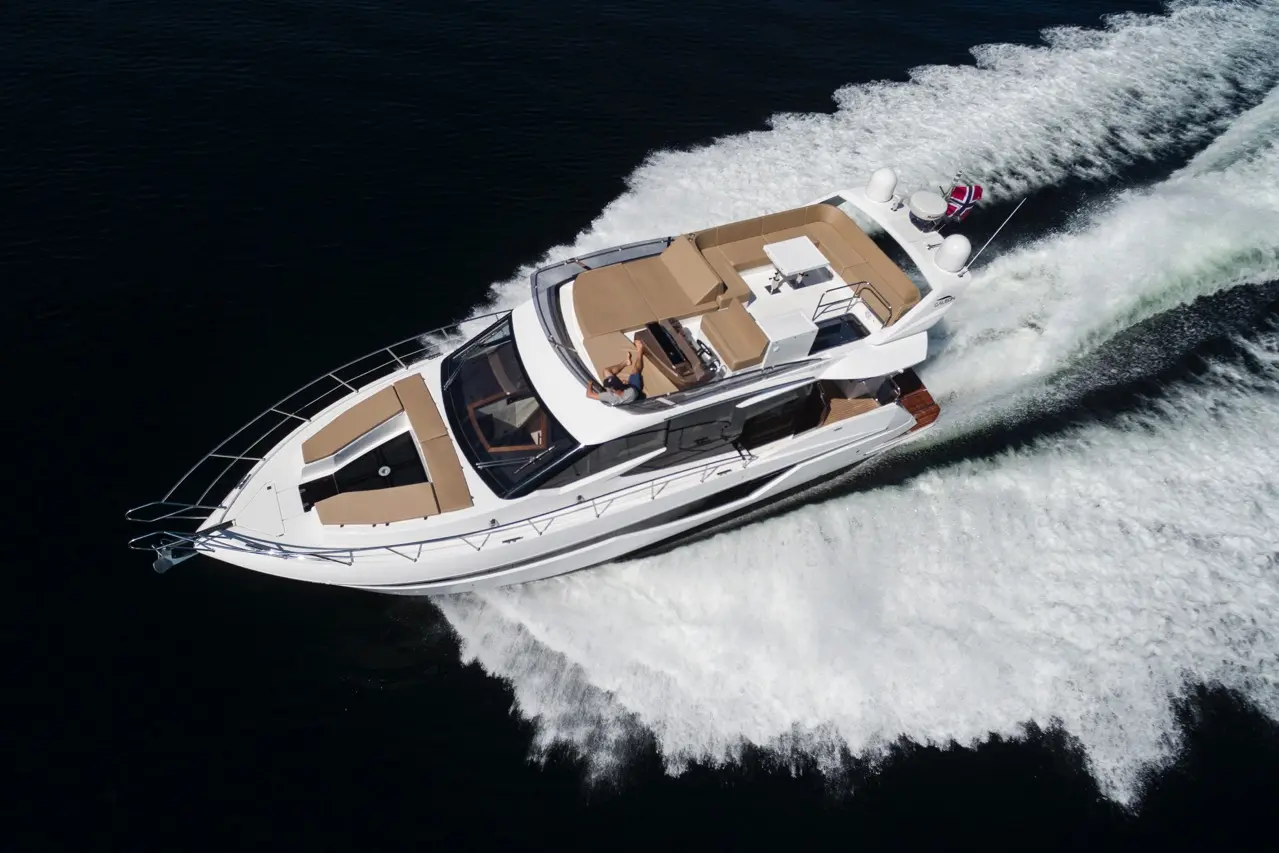 Luxury motor yacht gliding over dark waters, leaving a wake; a person lounges on the upper deck enjoying the sun.