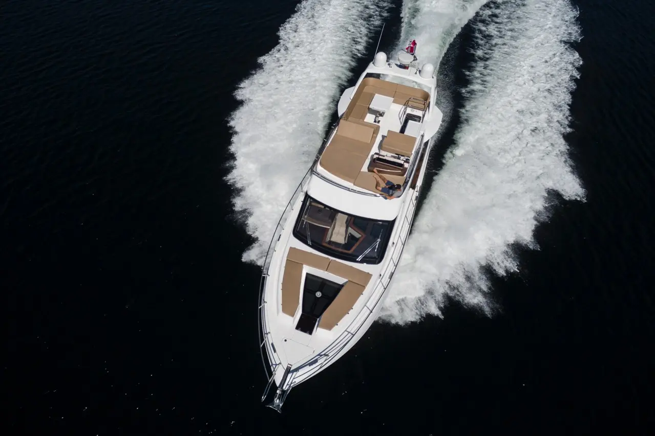 Luxury yacht cruising on dark water, leaving a trail of white foam; a person relaxes on the deck.