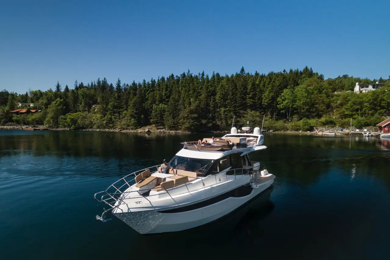 A luxurious motor yacht anchored in calm waters, surrounded by lush greenery and a scenic shoreline under a clear blue sky.