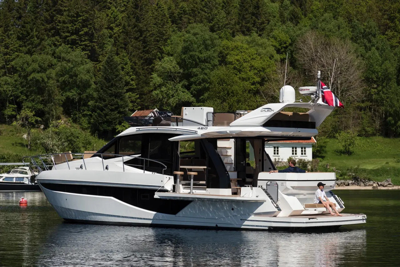 A luxury Galeon 460 Yacht docked in a serene bay, with a person relaxing on the deck surrounded by lush greenery.