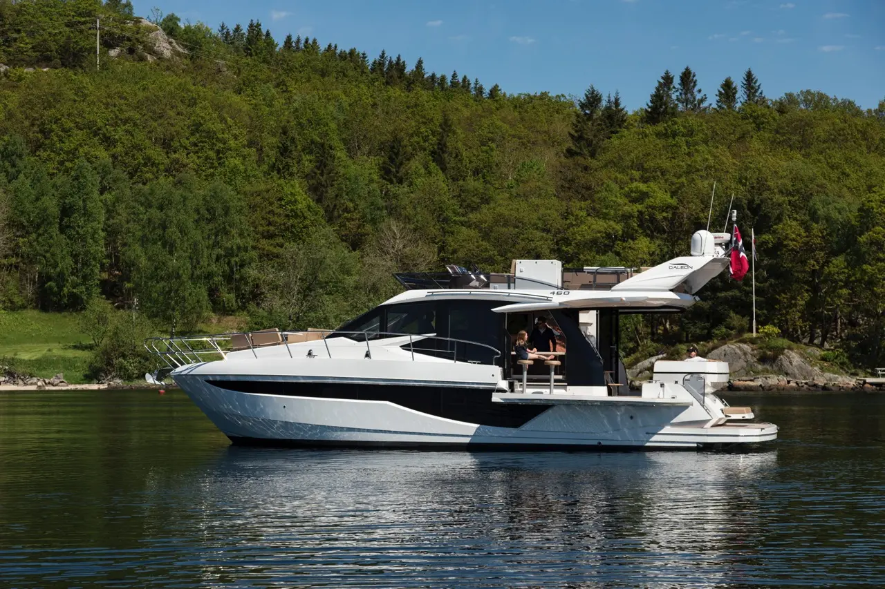 A luxurious motor yacht, model 460, glides on calm waters with passengers relaxing on deck amid lush greenery and blue skies.