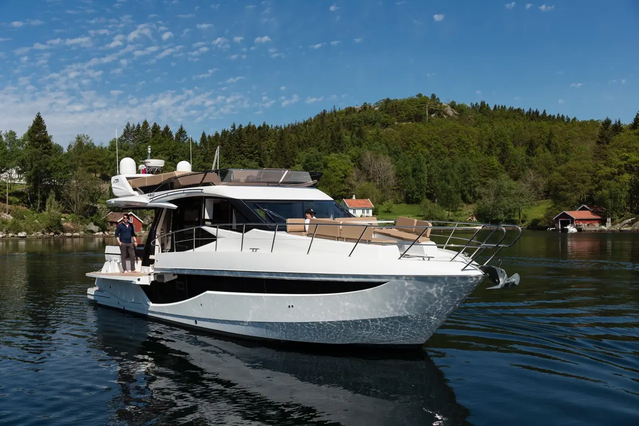 Luxury yacht anchored in a serene bay, with a person standing on the deck and another seated, surrounded by greenery.