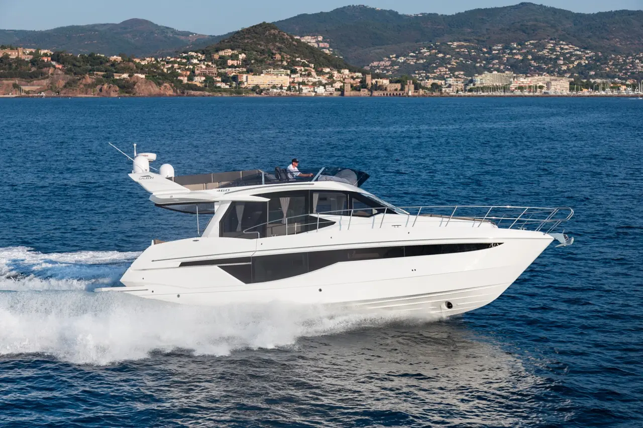 A sleek, luxurious white yacht cruising on calm blue waters, with a mountainous shoreline in the background.