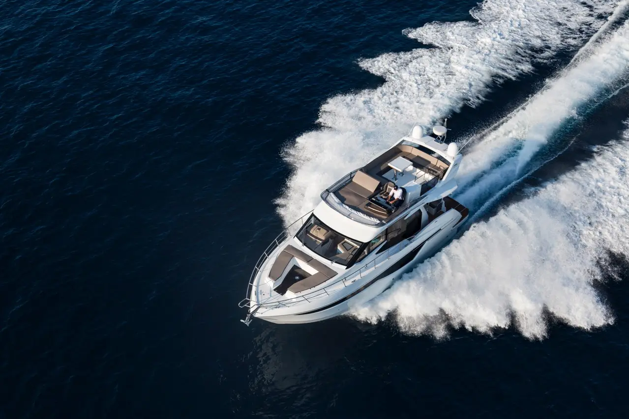 A sleek motor yacht cuts through deep blue waters, leaving a trail of white foam, with a person seated on the deck.