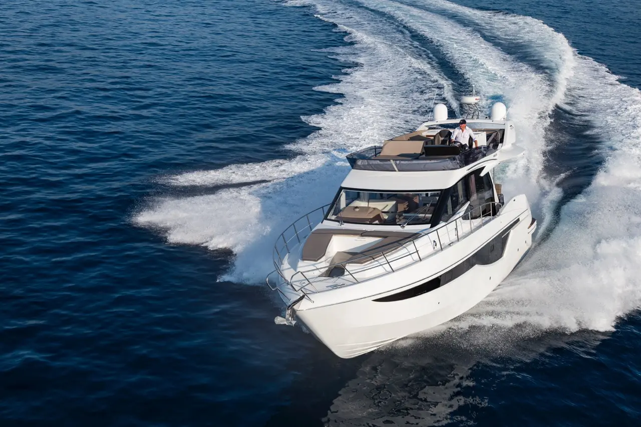 Luxury motorboat cutting through deep blue water, leaving a frothy wake with a person steering at the helm on a sunny day.