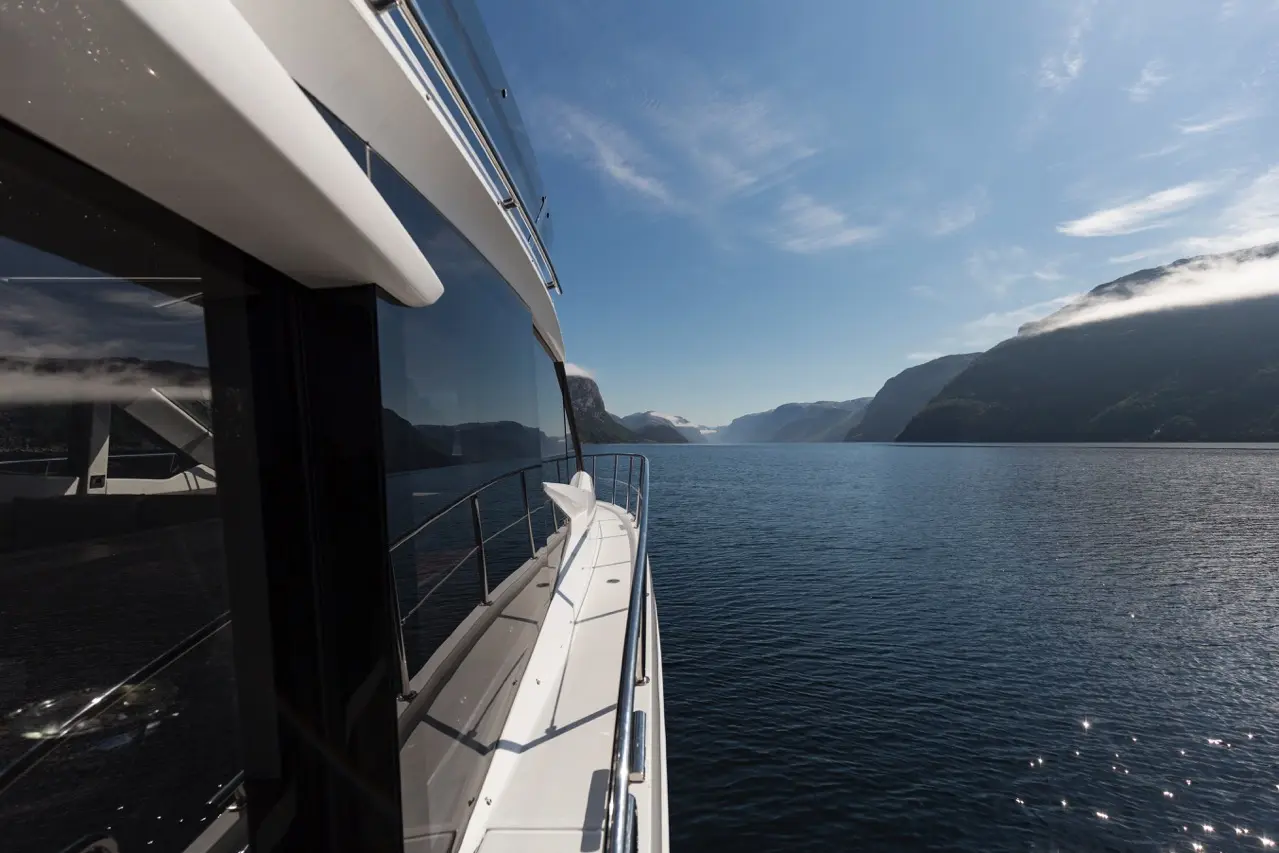 A luxurious yacht cruising through a serene fjord, showcasing clear skies and distant mountains reflecting on the water.