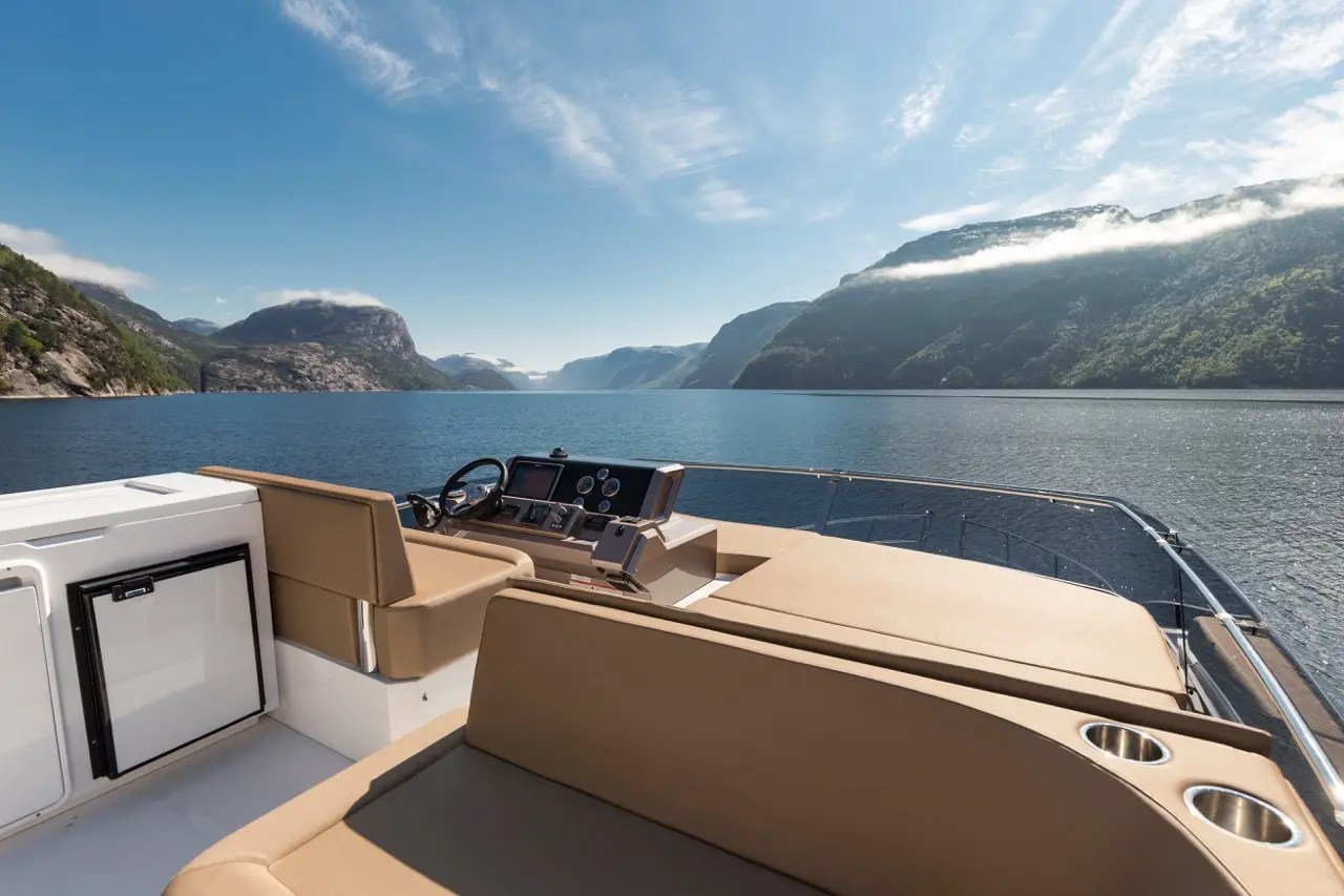 Scenic view from a boat showing a steering wheel, beige seating, and high cliffs surrounding a calm water fjord under a blue sky.