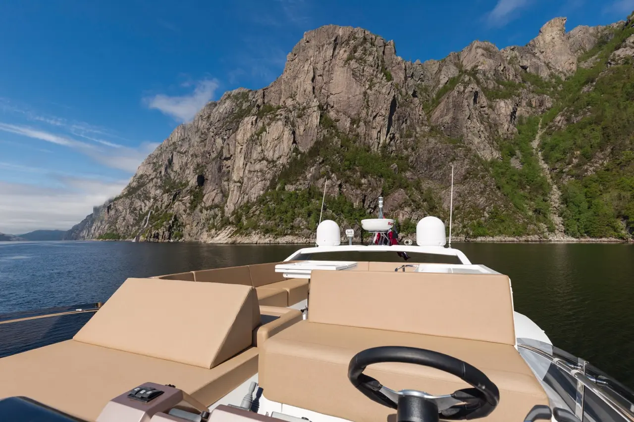 View from a luxury yacht, showcasing rocky cliffs, lush greenery, and calm waters under a blue sky.