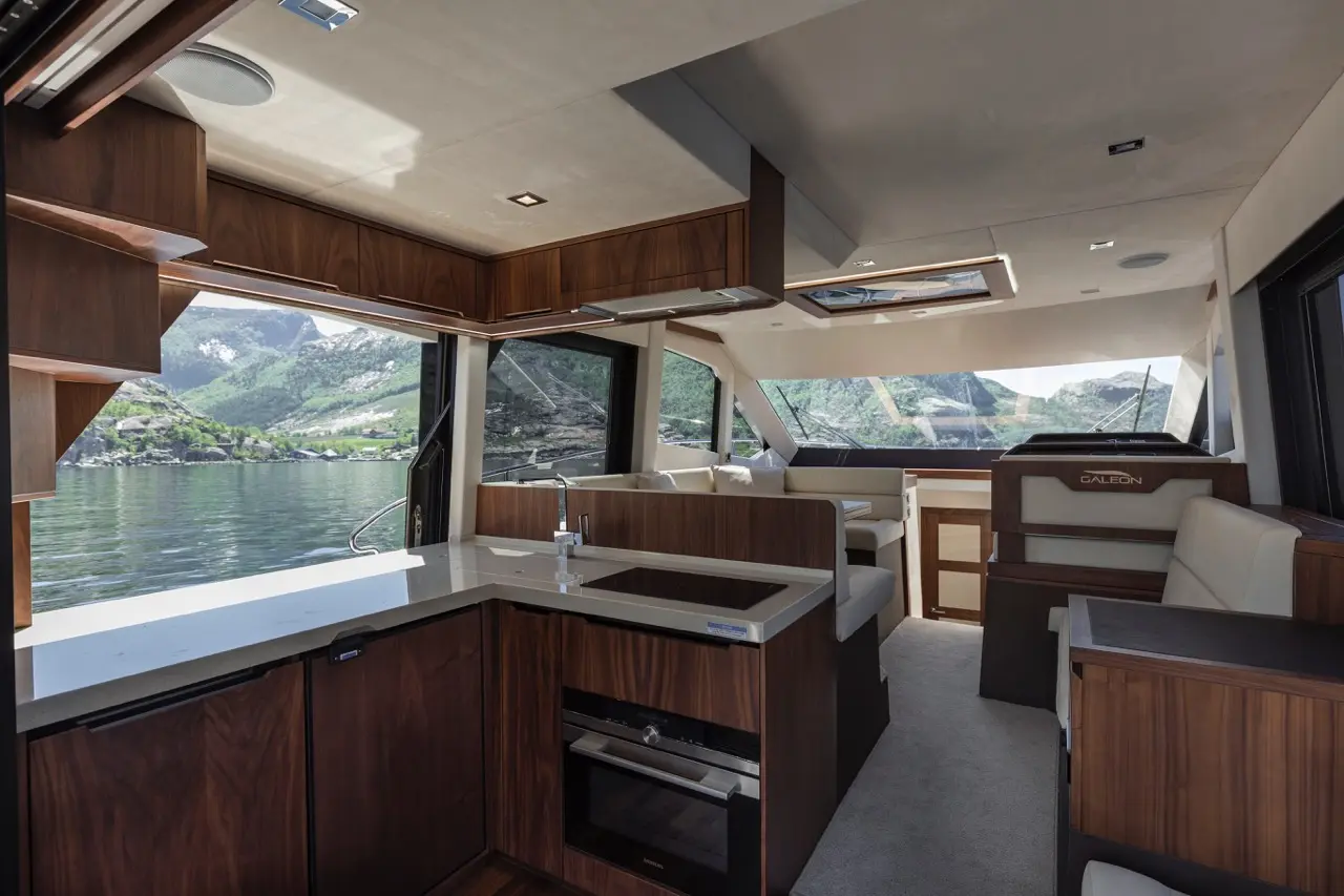 Modern yacht interior featuring a sleek kitchen area, plush seating, large windows, and mountain views.