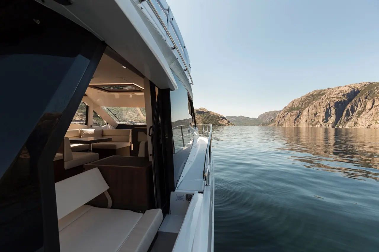 View from a luxury yacht showing a spacious interior with seating, overlooking calm waters and rocky hills in the distance.
